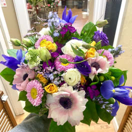 Hand-tied bouquet of purple iris, pink anemones, yellow roses, and assorted bright blooms.