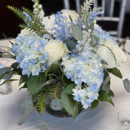 Blue hydrangeas and white roses arranged in a low centerpiece vase
