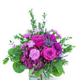 Low purple and pink rose arrangement in a clear glass vase with accent blooms