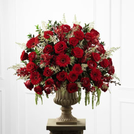 Large arrangement of red roses and gerbera daisies in a beige urn on a pedestal