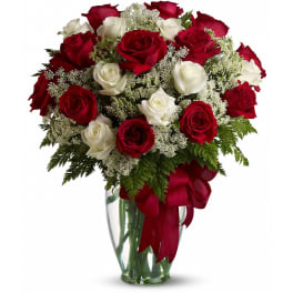 Bouquet of red and white roses with white filler flowers in a clear glass vase with a red bow