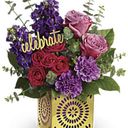 Pink and purple rose bouquet in a gold decorative box with a "celebrate" pick