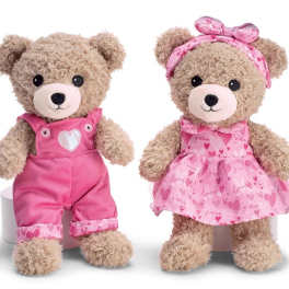 Two teddy bears in pink outfits, one in overalls and one in a dress