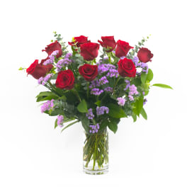Red roses and purple filler flowers in a clear glass vase
