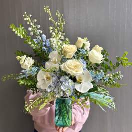 Bouquet of white roses, orchids, and blue flowers in a teal glass vase