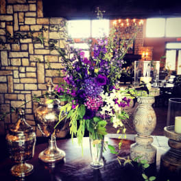 Tall purple and white floral arrangement in a clear vase