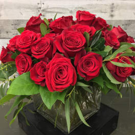 Red roses arranged in a clear square vase with greenery