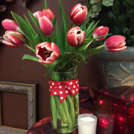 Red and white tulips in a clear vase with polka dot ribbon, next to a small white votive candle.
