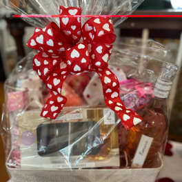 A gift basket wrapped in clear cellophane with a red heart ribbon and wine bottle.