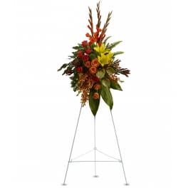 Tall standing spray of orange roses, yellow lilies, and other warm flowers on a metal easel