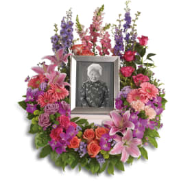 Wreath of pink and purple flowers with lilies and roses framing a silver photo frame