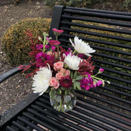 Pink and white flowers arranged in a clear glass vase on a black bench.
