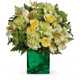 Arrangement of pale yellow roses, green carnations and alstroemeria in a green glass cube vase