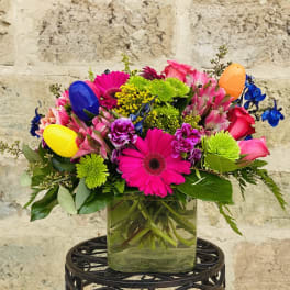 Bright mixed bouquet in a glass vase with colorful plastic eggs