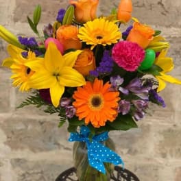 Bright mixed bouquet in a glass vase with a blue polka-dot ribbon