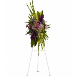 Tall standing spray of purple and green flowers displayed on a white metal easel.