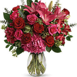 Bouquet of pink lilies, red roses, and hydrangeas in a clear glass vase