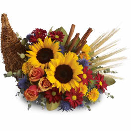 Cornucopia arrangement with sunflowers, orange roses, red daisies, and yellow mums with rustic accents.