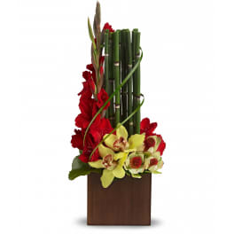 Tall modern arrangement with red flowers, green bamboo stalks, and yellow orchids in a brown square container