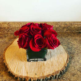 Red roses arranged in a square glass vase on a wood slice