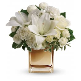 Compact white lily, rose, and carnation arrangement in a gold square glass vase