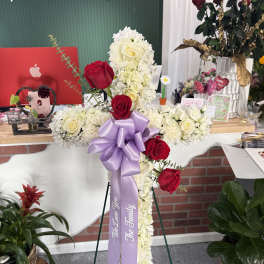 Cross-shaped floral tribute with red and white roses and a lavender ribbon