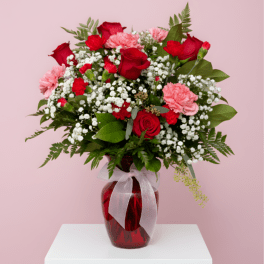 Red roses and pink carnations in a red glass vase with a white ribbon