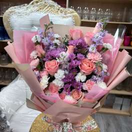 Hand-tied bouquet of pink roses, purple mums, and white and pink carnations wrapped in pink paper