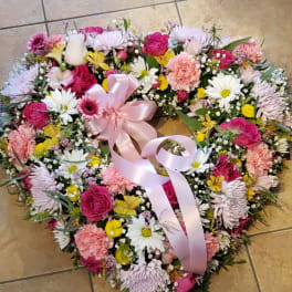Heart-shaped floral wreath with pink ribbon and mixed pink, white, and yellow flowers