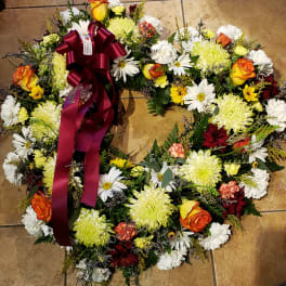 Round wreath of white, yellow, and orange flowers with a burgundy ribbon on a tile surface