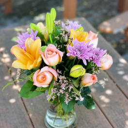 Bouquet of pink roses, yellow lilies, and purple chrysanthemums in a glass vase