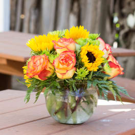 Bouquet of yellow sunflowers and peach-edged roses in a glass vase
