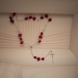 Red rose garland draped inside a white casket with a cross pendant
