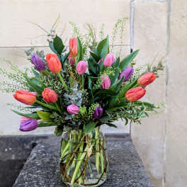 Mixed tulips in pink, purple, and orange arranged in a glass vase