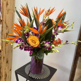 Orange bird of paradise bouquet with purple orchids in a vase