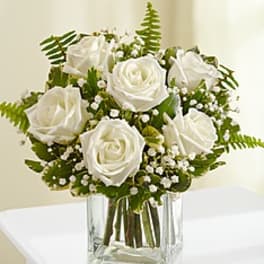 White roses arranged in a clear square vase with baby's breath