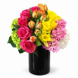 Bright mixed bouquet of roses, tulips, daffodils, and hyacinths in a black vase