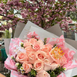 Peach rose bouquet wrapped in pink paper with a decorative crown accent.