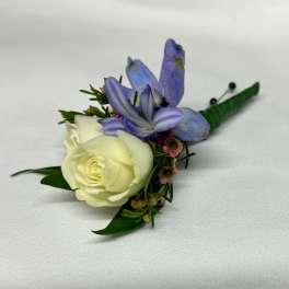 White rose boutonniere with purple flowers and green leaves