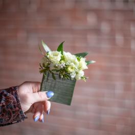 Small white floral corsage with green leaves on a wrist