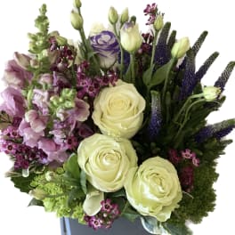 Bouquet of cream roses and purple flowers in a square vase