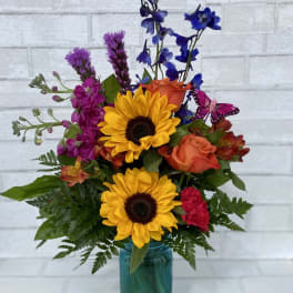 Colorful mixed bouquet in a teal glass vase with sunflowers and roses