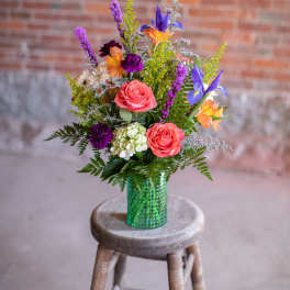 Colorful mixed bouquet in a green vase on a wooden stool