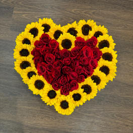 Heart-shaped arrangement of red roses bordered by yellow sunflowers