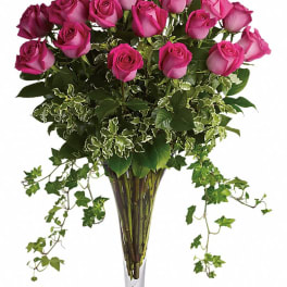 Pink roses arranged in a tall clear vase with trailing ivy