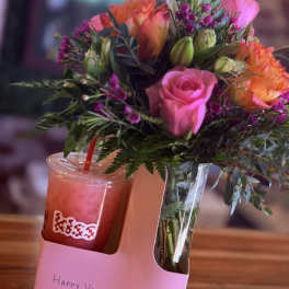 Pink and orange roses in a clear vase beside a pink drink cup.