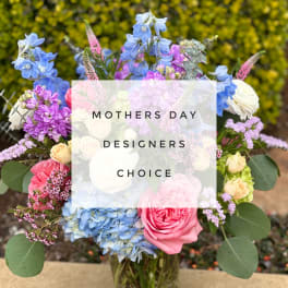 Mixed bouquet of blue, pink, purple, and cream flowers in a glass vase