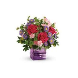 Bouquet of red roses and purple daisies in a purple square vase