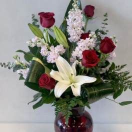Red roses and a white lily arranged in a burgundy glass vase