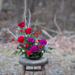 Red roses and purple flowers in a low black bowl with a "Love" pick